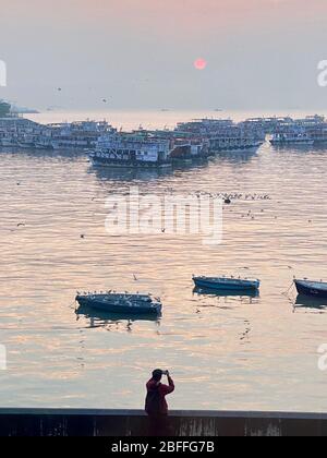 Homme prenant la photo du lever du soleil et des bateaux à travers le smog à Mumbai. Banque D'Images