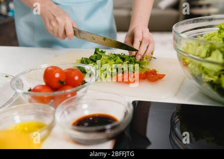 Gros plan de salade verte coupée à bord. Mains féminines préparer une salade verte fraîche et mettre les ingrédients dans un bol transparent sur le fond de la cuisine. Banque D'Images