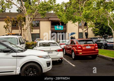 Un ministre dans un service de Pâques en voiture dans un parc de bureaux de Santa Ana, Californie, parle d'un balcon de deuxième étage avec une bannière disant "il est ressuscité". Le service de drive-in a été provoqué par l'éclosion de coronavirus ou COVID-19 Banque D'Images