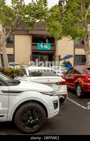 Un ministre dans un service de Pâques en voiture dans un parc de bureaux de Santa Ana, Californie, parle d'un balcon de deuxième étage avec une bannière disant "il est ressuscité". Le service de drive-in a été provoqué par l'éclosion de coronavirus ou COVID-19 Banque D'Images