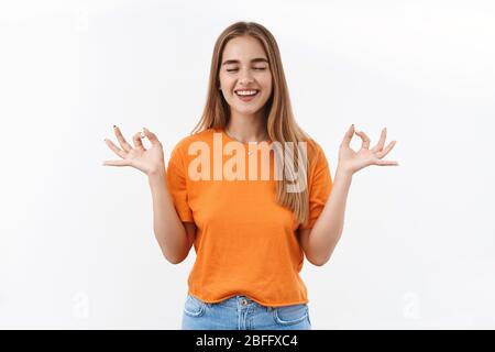 Soulagé fille heureuse essayant la méditation pendant le verrouillage de Covid-19, garder calme et paisible. Femme blonde faire du yoga, atteindre le nirvana, respirer et sourire avec Banque D'Images