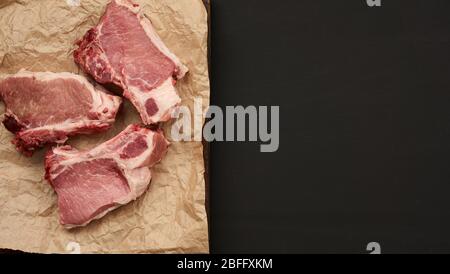tranches de porc juteux cru de viande sur la côte, la nourriture se trouve sur du papier parchemin brun, sur fond de bois noir et un espace vide pour écrire une recette ou un menu Banque D'Images