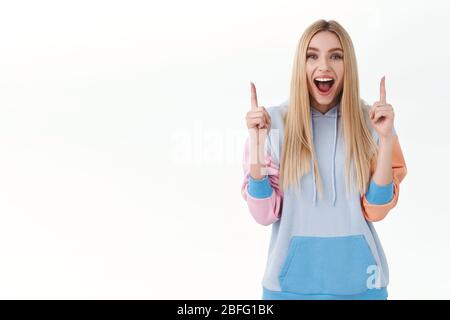 Gai bonne-look blonde fille à capuche trouvé meilleure offre, des réductions sur le site de shopping, offre en ligne de promotion, pointant les doigts vers le haut à la bannière, montrant Banque D'Images