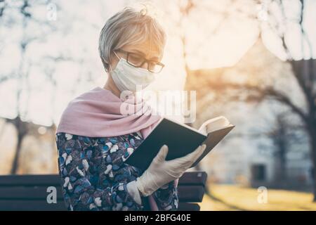 Dame senior avec masque de visage lisant la bible devant une église Banque D'Images