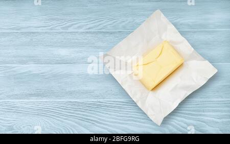 Morceau de beurre sur le papier d'emballage isolé sur fond bleu en bois. Vue de dessus du beurre. Banque D'Images