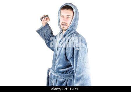 Portrait de jeune homme caucasien barbu dans un peignoir bleu frappe avec un porte-fusée en laiton dans sa main sur fond blanc. Agrésion et violence familiale conc Banque D'Images