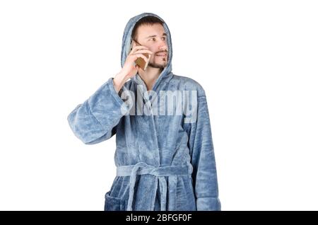 Portrait de jeune homme caucasien barbu dans un peignoir bleu parle sur smartphone isolé sur fond blanc. Concept de conversation téléphonique Banque D'Images