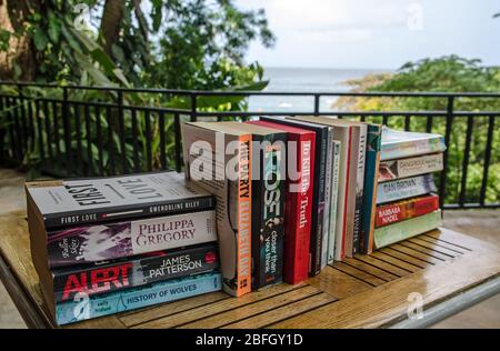 Castara, Trinité-et-Tobago - 12 janvier 2020: Une sélection de livres de fiction populaires sur le dos de papier assis sur une terrasse surplombant la mer des Caraïbes. Banque D'Images