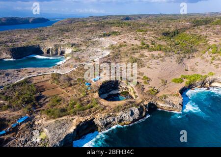 Vue aérienne des vagues de l'océan qui s'écrasent par une voûte rocheuse dans une baie isolée ronde (plage cassée, Nusa Penida, Indonésie) Banque D'Images