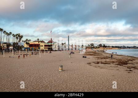 Vue sur la plage principale en soirée, avec palmiers en rangée, terrains de volley et personnes. La promenade de Santa Cruz Beach est en arrière-plan. Banque D'Images