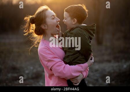 Gros plan sur une belle mère et son fils s'amuser en plein air. Un petit mignon petit enfant a été hoché par sa mère dans les bras qui rient contre le coucher du soleil. Mère Banque D'Images