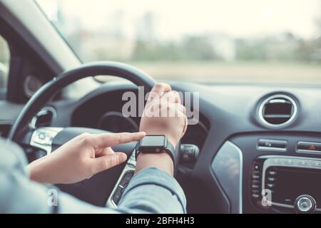 Gros plan sur la femme en utilisant la montre intelligente pendant la conduite de sa voiture, concept de transport Banque D'Images