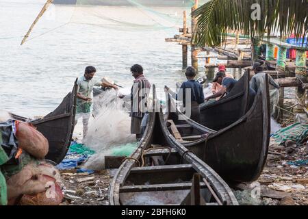 Kochi, Kerala - 30 décembre 2019: Les pêcheurs qui enmentent leurs filets à côté de leurs bateaux de pêche à fort kochi, kerala inde Banque D'Images