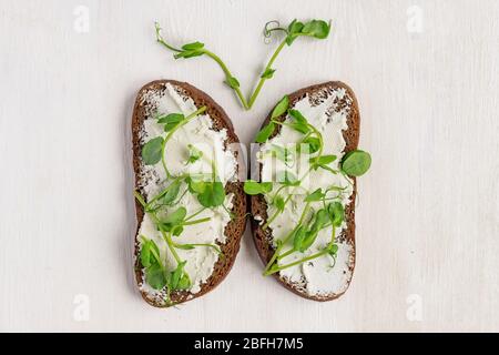 Deux sandwichs à base de pain de seigle foncé avec fromage à la crème frais et microgreens aux pois biologiques verts. Petit déjeuner sain. Vue de dessus Banque D'Images