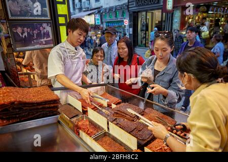 Les assistants de magasin aident leurs clients à choisir parmi une sélection de jerkies de viande traditionnels macanais sucrés et épicés. Macao, Chine. Banque D'Images
