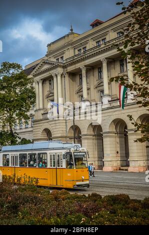 Budapest, Hongrie - 6 novembre 2019 : tramway jaune devant le bâtiment du Ministère de l'agriculture. Ciel spectaculaire avec nuages de tempête. Place Kossuth au centre. Photo verticale. Banque D'Images