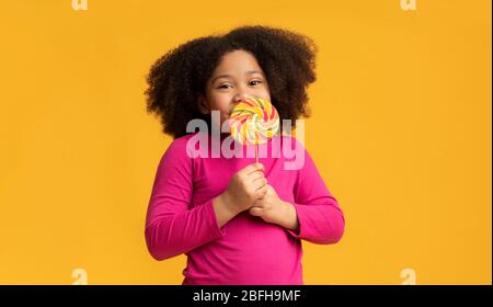 Positive petite afro fille régaler des bonbons à la lollipop, en appréciant le sucre traiter Banque D'Images