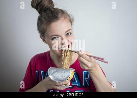 Young caucasian girl woman eating instant ramen noodles with chopsticks Banque D'Images