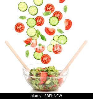 Légumes frais mélangés qui tombent dans un bol de salade isolé sur blanc Banque D'Images