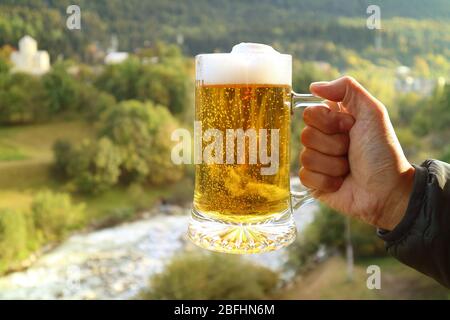 Pinte de bière dans la main de l'homme contre la vue brouillée de la forêt de pied dans la lumière du soleil du soir Banque D'Images