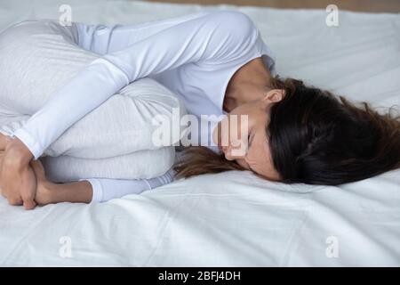 Gros plan femme mécontente posée dans le lit en position fœtale Banque D'Images