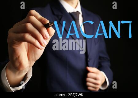 Homme d'affaires qui écrit VACANT sur un tableau blanc transparent, gros plan Banque D'Images