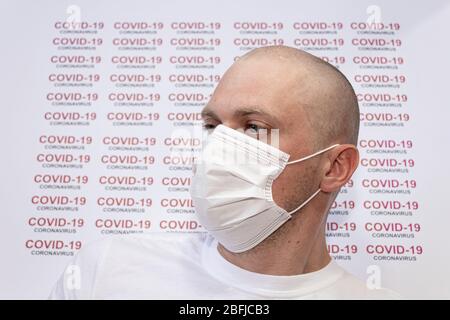 Coronavirus. Convid-19. Un malade médical porte un masque facial avec du texte COVID-19 coronavirus sur fond blanc. Un homme chauve dans sa trentaine. Banque D'Images