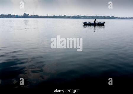 Un pêcheur inreconnaissable sur son bateau vu de loin, sans aucune autre personne, près du quartier historique de Kochi, Kerala, Inde Banque D'Images