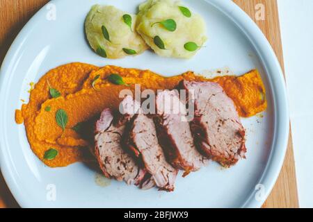 Filet de porc dans une assiette de crème de carottes et de fruits frais Banque D'Images
