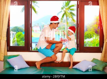 père présentant son fils une savoureuse bonbons à noël, tout en étant assis sur le seuil de vent dans les tropiques Banque D'Images