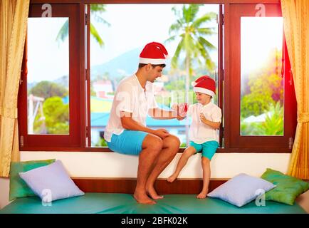 père présentant son fils une savoureuse bonbons à noël, tout en étant assis sur le seuil de vent dans les tropiques Banque D'Images