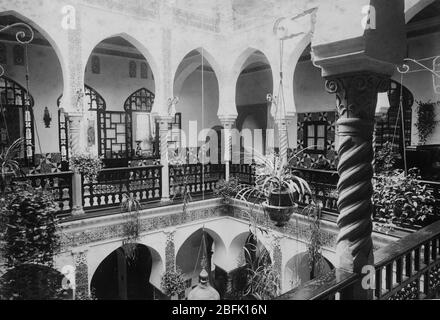 Une belle maison Riyad à Alger, Algérie française, Afrique. Cette vue est d'un balcon sur la cour intérieure, qui est un jardin suspendu virtuel. Il y a des rangées de livres à l'intérieur de la porte sombre à travers le balcon. Les années 1880 ou 1890 Pour voir mes autres lieux-images vintage liées, recherche : Prestor vintage Places African Banque D'Images