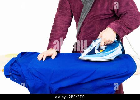 homme dans un peignoir rouge repassage une chemise bleue Banque D'Images