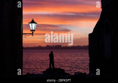 Une silhouette solitaire au coucher du soleil en regardant sur la bande de 2 km de mer de l'île de Gorée à Dakar sur le continent Sénégal. Banque D'Images