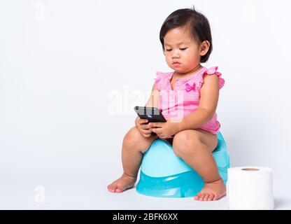 Asiatique petite mignonne bébé fille éducation entraînement à s'asseoir sur pot bleu de chambre ou pot et jouer smartphone mobile avec des rouleaux de papier de toilette, goujon Banque D'Images