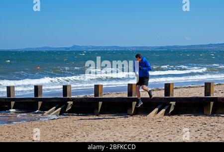 Plage de Portobello, Édimbourg, Écosse. 19 avril 2020. Les gens qui font leurs exercices quotidiens sur la plage par temps ensoleillé, une nageur sauvage féminine bravant le surf fraisky, moins de gens qu'hier, comme le Lockdown de Coronavirus continue, Cependant, la Promenade était animée avec des cyclistes comme toujours, plus que la plage, bien que la plage de sable puisse être plus facile pour les marcheurs à s'isoler. Température de 10 degrés avec un vent ENE de 17 km/h de rafale potentielle de 33 km/h. Crédit: Arch White/Alay Live News. Banque D'Images