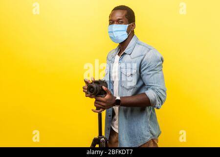 Portrait d'un photographe motivé excité ou blogueur vidéo avec masque médical chirurgical souriant et à l'appareil photo avec appareil photo numérique professionnel reflex numérique activé Banque D'Images