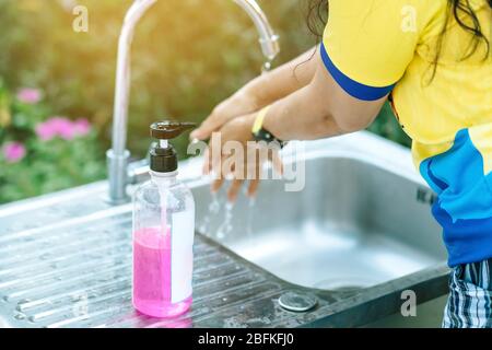 Une femme se lavant les mains du robinet avec du savon rose dans une baignoire en aluminium. Concepts du virus de la grippe, Covid-19 (maladie du coronavirus). Focalisation sélective sur le savon b Banque D'Images