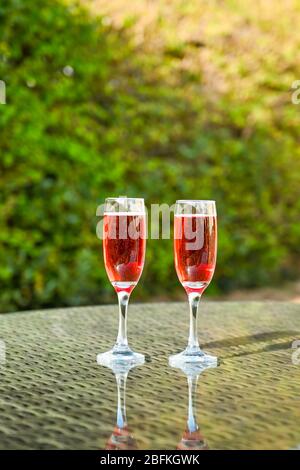 Champagne rose dans deux flûte à verres côte sur un plateau de table en verre dans un jardin Banque D'Images