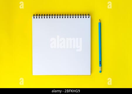 Cahier pour dessiner ou écrire sur un fond jaune avec différents accessoires de papeterie. Banque D'Images