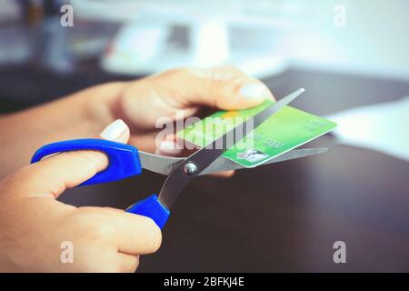 Les mains de la femme coupants la carte de banque avec des ciseaux sur fond de table en bois Banque D'Images