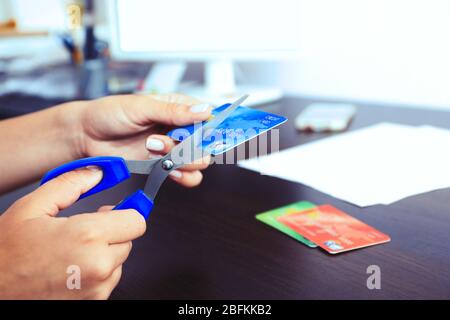 Les mains de la femme coupants la carte de banque avec des ciseaux sur fond de table en bois Banque D'Images