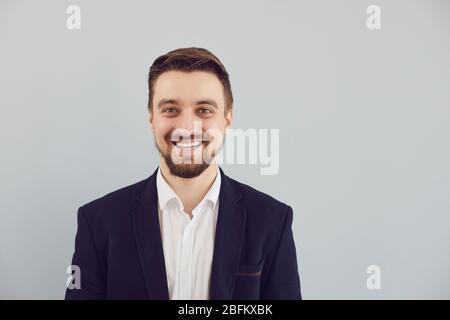Un gars à barbe positive dans une veste souriant regarde l'appareil photo sur un fond gris. Banque D'Images