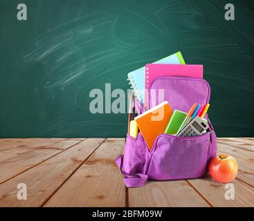 Sac à dos avec fournitures scolaires sur table en bois sur fond vert de bureau Banque D'Images