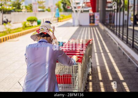 Une employée femelle collecte des chariots à l'extérieur d'une succursale de la chaîne de supermarchés Banque D'Images