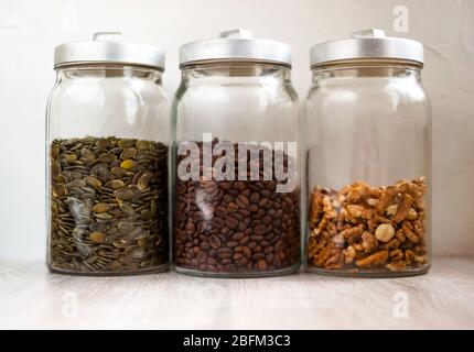 Grains de café, graines, noix en pots de verre, couvercles métalliques sur fond rustique blanc de la cuisine en bois Banque D'Images