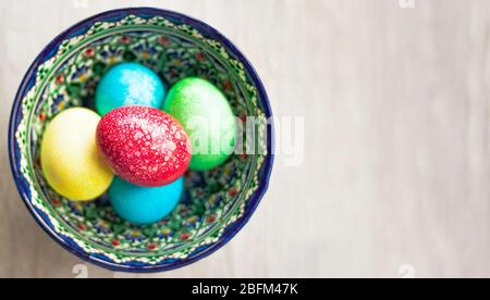 Œufs de Pâques colorés dans un bol sur fond blanc naturel en bois. Vue de dessus. Pose plate. Banque D'Images