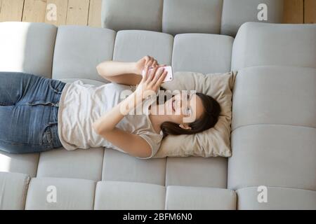 Jeune femme souriante en utilisant un smartphone allongé sur un canapé. Banque D'Images