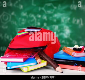 Sac rouge avec équipement scolaire sur table en bois près du tableau noir Banque D'Images