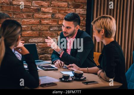Divers collègues, partager leurs idées sur le projet et analyser les statistiques et la stratégie tout en appréciant leur café dans un café. Banque D'Images